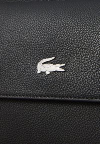 Svart texturerad lädersurface med en liten silverfärgad krokodil-logotyp. Enkelt design med fina detaljer på logotypen och materialet.