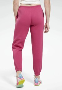 Dresy z polaru w intensywnie różowym kolorze z bocznymi kieszeniami i elastycznymi mankietami, w zestawieniu z wielokolorowym obuwiem sportowym z siateczki i gumowej podeszwy.