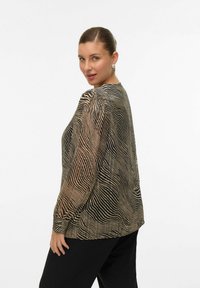 Blouse à manches longues rayée noire et beige avec un col rond et un tissu texturé. Épaules accentuées et coupe décontractée.