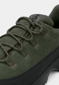 Scarpa da trekking verde con tomaia morbida e testurizzata, suola in gomma nera e lacci sottili rinforzati, assicurati tramite anelli di tessuto.