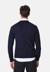 Maglione lavorato a maglia blu navy che presenta una combinazione di trame, inclusi motivi a treccia e orli a coste, con scollatura tonda e maniche lunghe.