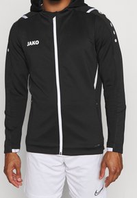 Svart zip-up hoodie i texturerad tyg, med en vit dragkedja, logotyp på bröstet, samt vita och grå detaljer på axlarna.