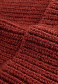 Teksturirani pleteni materijal u dubokoj crvenoj boji, s uzdignutim rebrima i mekim, izblijedjelim izgledom. Pogodan za tople odjevne predmete ili dodatke.