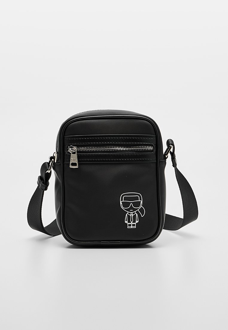 Bolso bandolera negro hecho de material liso que presenta un bolsillo frontal con cremallera y un diseño de personaje de dibujos animados blanco en el lateral.