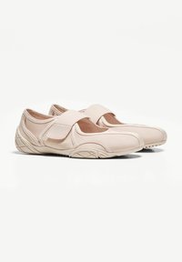 Pantofi slip-on de un bej deschis, cu panouri din plasă, bretele elastice și talpă din cauciuc texturat. Proiectați cu un vârf rotunjit și o formă conturată.