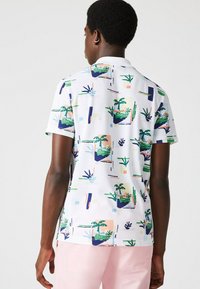 Polo à manches courtes en blanc avec un motif botanique coloré comprenant des plantes, des formes abstraites et des accents géométriques.