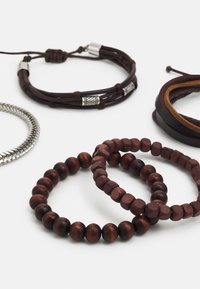Ensemble de cinq bracelets en cuir, argent et bois. Perles marron foncé dans deux styles, cuir tressé et accents métalliques. Finitions texturées.