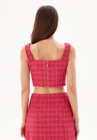 Top corto in tweed rosa con scollatura quadrata, spalline spesse e zip dorata sul retro. Tessuto strutturato con orlo leggermente sfrangiato.