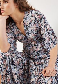 Blümchenkleid in Marineblau mit rosa und blauen Blumenmustern. Merkmale sind ein tiefer V-Ausschnitt und fließende Ärmel, aus leichtem Stoff gefertigt.