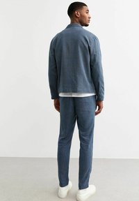 Blauwe corduroyjas en bijpassende broek met verticale strepen. Beschikt over een casual pasvorm, textuurstof en witte sneakers.
