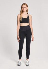 Brassiere sportivo nero e leggings a vita alta, entrambi realizzati in materiale liscio e elastico. Abbinati a scarpe da ginnastica argento.