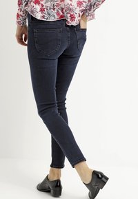 Jeans ajustados de mezclilla en color azul oscuro, con una cintura baja-media, bolsillos traseros y un corte ajustado, combinados con tacones negros.