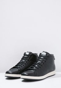 Svarta hög-top sneakers i läder, med en slät yta, vit gummisula, snörningsdesign och accentlogotyp på tungan.