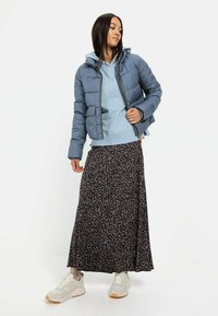 Polstret blå jakke med hætte, over en lyseblå hoodie og en blomsterpræget maxi-nederdel. Grå sneakers med beige detaljer.