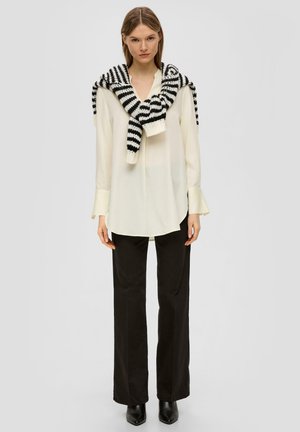 White long-sleeve blouse accompanied by a black-and-white striped knit sweater draped casually over the shoulders; paired with black trousers.
