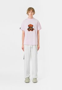 Camiseta de manga corta rosa con un gráfico de un oso marrón y negro, combinada con pantalones cargo blancos y zapatos verde claro texturizados.