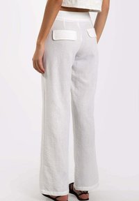 Pantalones de lino blancos de pierna ancha con cintura alta, bolsillos traseros con solapas y una textura suave. El dobladillo se encuentra cerca del tobillo.