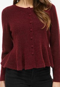 Bordowy sweter kardigan z okrągłym dekoltem, zapinany na siedem guzików, z peplum na dole. Miękka faktura i długie rękawy.