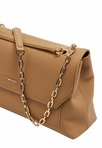 Borsa a tracolla in finta pelle marrone con texture, dotata di una tracolla in catena dorata e chiusura piatta. Presenta un logo discreto sul davanti e una forma angolare.