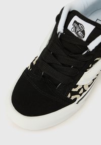 Ασπρόμαυρο αθλητικό παπούτσι με επάνω μέρος από υφή σουέντ, λεπτομέρειες σε σχέδιο λεοπάρδαλης και λευκή λαστιχένια σόλα με κλασικό σχέδιο δεσίματος με κορδόνια.