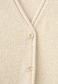 Gros plan d’un cardigan tricoté couleur crème avec deux boutons beige et un col en V.