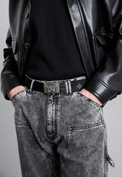 Zwarte leren jas over een zwart geribd topje, gecombineerd met grijze denim broek. Heeft een zilveren gesp riem en opvallende stiksels.