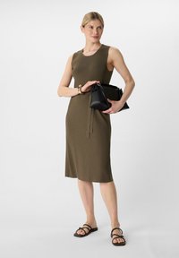 Olivgrünes, geripptes Kleid mit tailliertem Oberteil und weit ausgestellt am Saum. Kombiniert mit einer schwarzen Ledertasche mit gerafftem oberen Teil und schlichten Sandalen.