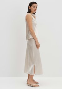 Top sans manches en satin crème et jupe longueur cheville assortie, avec une fente latérale, texture lisse et design minimaliste. Sandales plates.