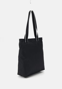 Sac fourre-tout en tissu noir avec deux longues anses. Présente une texture lisse et des coutures blanches contrastantes le long des bords des anses.