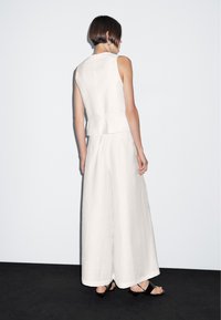 Vit linnetopp utan ärmar med en peplummidja, i kombination med vida vita byxor. Platta svarta sandaler. Minimalistisk design, slät textur.