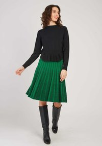 Un pull en tricot noir avec un ourlet évasé associé à une jupe plissée verte avec un motif à carreaux. Des bottes noires montantes complètent le look.