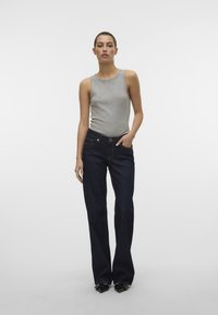 Top gris sin mangas con escote redondo, combinado con jeans de campana azul oscuro y tacones de punta negra. Texturas suaves, ajuste casual.