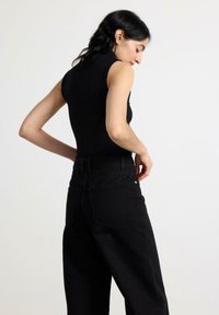 Sort ribbet bluseløs top parret med højtaljede sorte jeans. Stoffet ser glat ud med subtil tekstur og har minimalistiske designdetaljer.