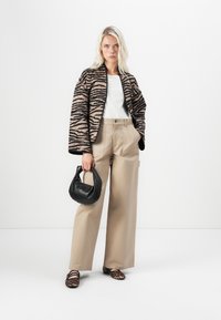 Zebra-gepatenteerde jas in beige en zwart, witte top, beige wijde broek, zwarte handtas en schoenen met luipaardprint. Gladde texturen overal.