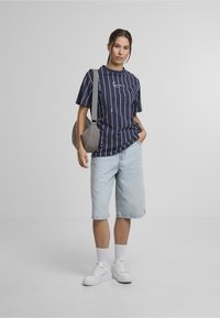 Marineblå T-shirt med hvide striber, kombineret med lyseblå denimshorts. Hvide sneakers og en quiltet grå skuldertaske.