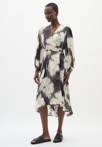 Rochie tip wrap dintr-un material ușor, cu imprimeu abstract în alb și negru, mâneci lungi și talie ajustată. Asortată cu sandale negre cu talpă plată.
