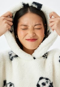 Sudadera blanca y esponjosa con patrones de panda negros y una gran capucha. La textura parece suave, lo que enfatiza la calidez y la comodidad.