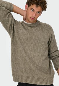 Suéter de punto grueso y acanalado en color oliva apagado. Cuello redondo, corte relajado con hombros caídos y puños enrollados. Tela texturizada.