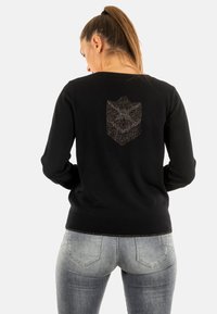 Pull noir avec un col rond et des manches longues. Présente un motif géométrique texturé au dos. Le matériau semble doux et extensible.