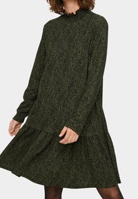 Mörkgrön klänning med långa ärmar i ett tyg med en texturerad zigzag-mönster, som har en volangkrage och en flerskiktad nederkant.