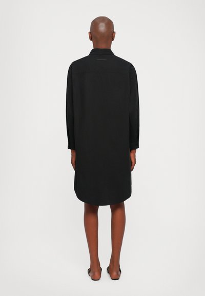 Black long-sleeve shirt dress with a collared neckline, relaxed fit, smooth texture, and a slightly curved hem. Features minimal detailing.