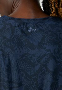 Marineblå top med et subtilt slangeskinds mønster, glat tekstur, rund halsudskæring og små runde detaljer nær ryggen.