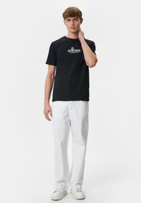 Sort bomulds t-shirt med rund hals og korte ærmer, prydet med hvid tekst. Kombineret med hvide lige ben bukser og hvide sneakers.