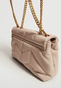 Sac à main beige matelassé avec une texture douce, présentant un sommet roulé et des bandoulières en chaîne dorée. Les détails incluent une couture en motif géométrique.