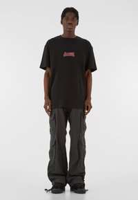 Must rehvus T-särk mustas värvitoonis, millel on punane graafikatekst rinnal, koos tumehallide cargo-pükstega, millel on mitu taskut ja vabalt langev lõige.