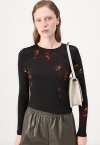 Svart langermet topp med blomsterprint i rødt og gult, kombinert med olivengrønne plisserte bukser og en beige håndveske. Glatt stofftekstur.