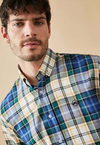 Camisa de cuadros con patrones en azul, verde, amarillo y blanco; cuello abotonado; tela suave; ligero brillo; detalle del logo en el pecho.