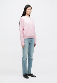 Pulover roz deschis cu mâneci lungi, gât rotund și mansete cu nervuri; asortat cu blugi drepti de culoare albastră deschisă și pantofi negri fără șireturi.