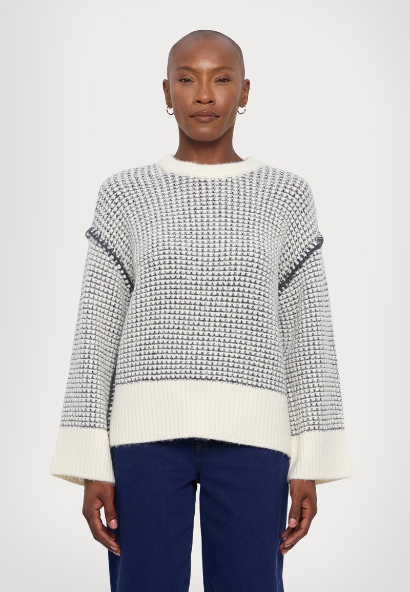 Chunky knit sweater in cream and grey, featuring a textured pattern, wide sleeves, and a ribbed hem. Soft material with relaxed fit.