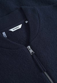 Mornarsko modra flis jakna z zaobljenim ovratnikom, ki ima srebrno zadrgo in oznako z napisom "GABBA". Mehak tekstura brez vidnih vzorcev.